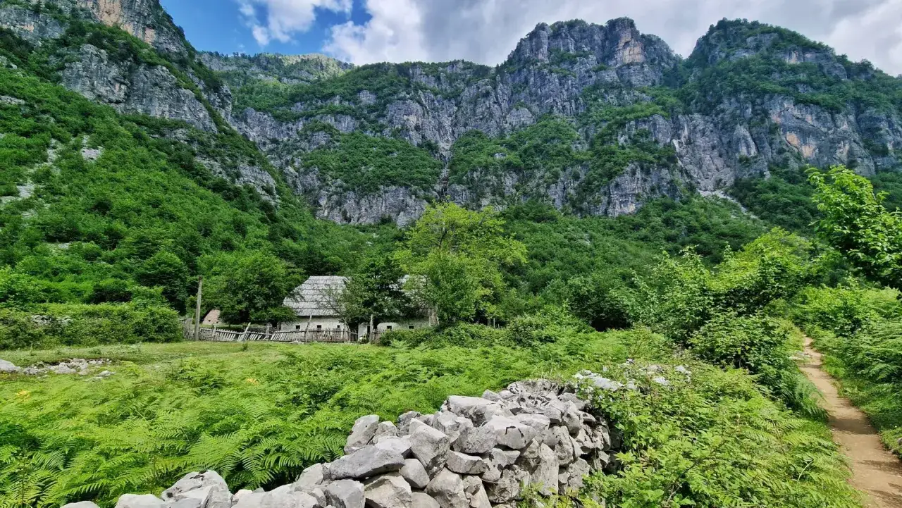Kamienny murek i ścieżka prowadzą do tradycyjnego domu w Theth, Albania, otoczonego bujną zielenią i majestatycznymi górami.