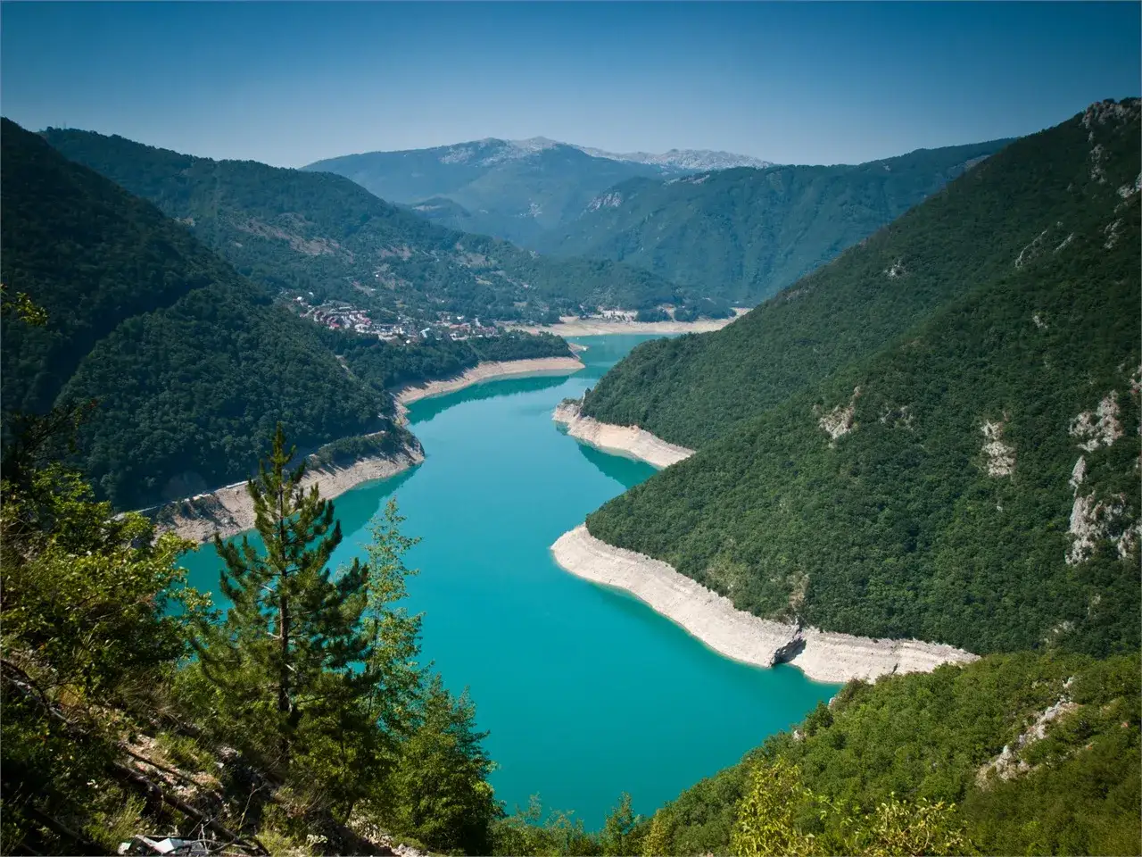 Turkusowe Pivsko Jezero otoczone zielonymi górami, z widocznym miasteczkiem na brzegu.