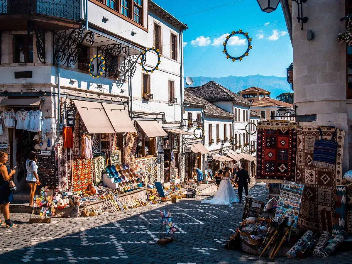 Ulica w Gjirokastrze, Albania, pełna kolorowych dywan&oacute;w i pamiątek. Czy Albania jest droga? Zakupy tutaj wydają się przystępne.