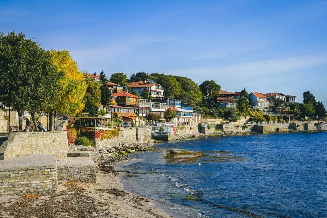Urokliwy widok na wybrzeże w Nesebyrze. Kamienne mury, plaża i domy na wzgórzu nad błękitnym morzem.