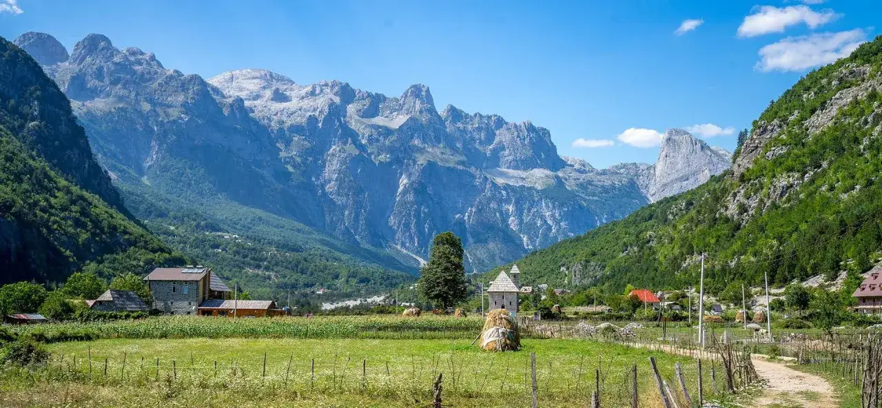 Majestatyczne, skaliste góry przeklęte górują nad zieloną doliną z domkami i stogami siana.