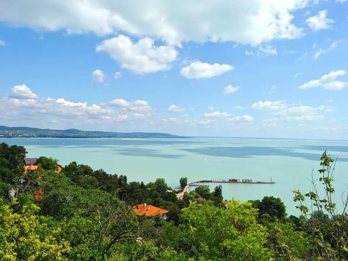 Widok na turkusowe wody Balatonu na Węgrzech, z zielonymi wzgórzami i domami w tle.