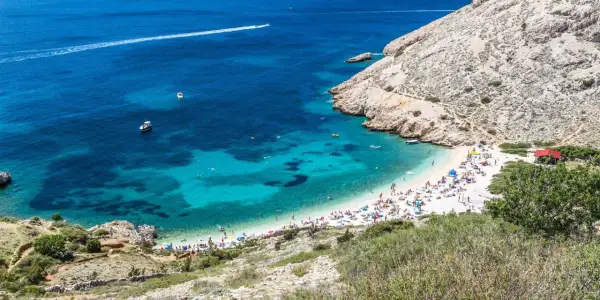 Rajska plaża w Baška Chorwacja, z turkusową wodą, łodziami i mnóstwem plażowiczów.