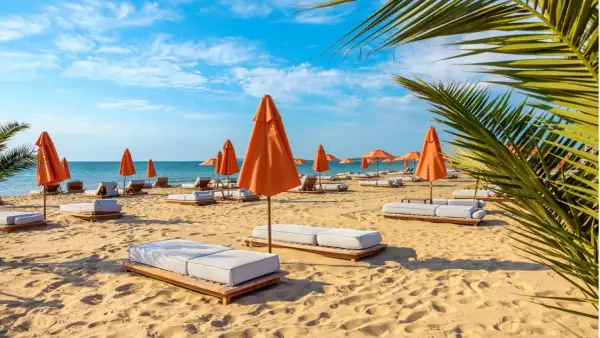 Słoneczny dzień na plaży z pomarańczowymi parasolami i leżakami na złotych piaskach. Błękitne niebo i spokojne morze zapraszają do relaksu.