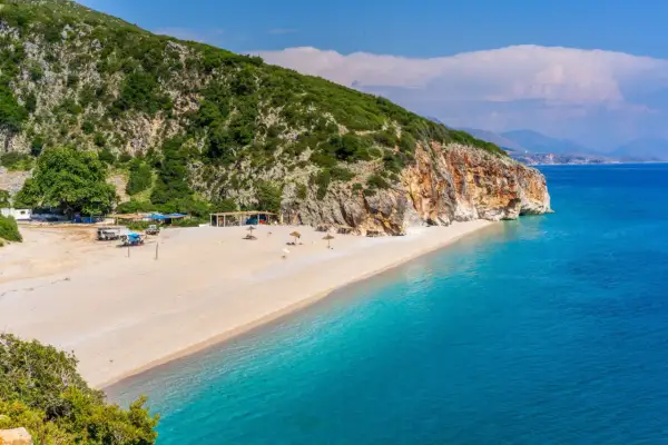 Piękna plaża Dhermi z turkusową wodą, skalistym klifem i zielonymi wzgórzami.