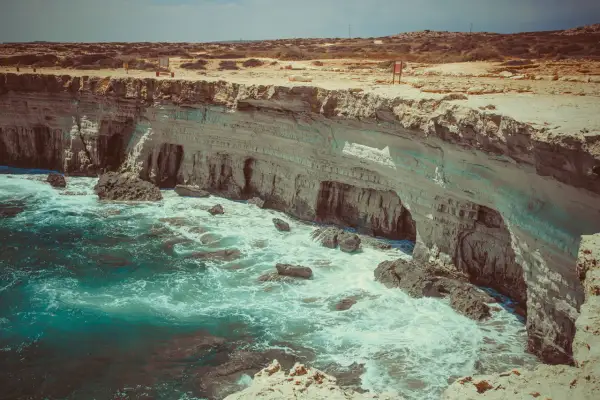 Wysokie klify i turkusowe morze przy Cape Greco na Cyprze. Fale rozbijają się o skały.