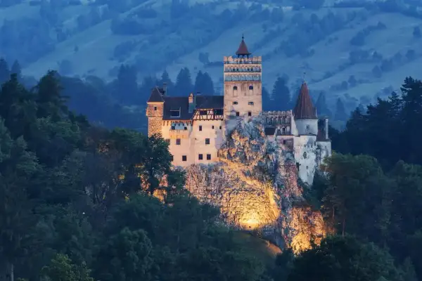 Zamek Bran w Transylwanii, oświetlony nocą, na tle zalesionych wzgórz.