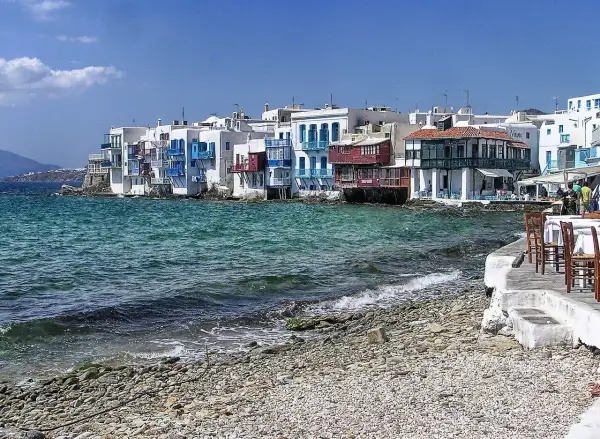 Malownicze Mykonos: białe domy z niebieskimi okiennicami nad turkusowym morzem. Warto sprawdzić mykonos ceny przed podróżą.