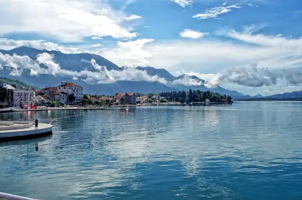 Widok na spokojną kotor zatoka z górami w tle i miasteczkiem nad brzegiem.