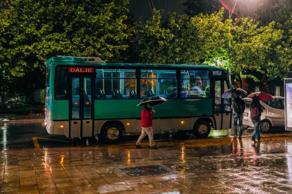 Deszczowa noc w Tiranie. Ludzie z parasolami czekają na autobus do Durrës.