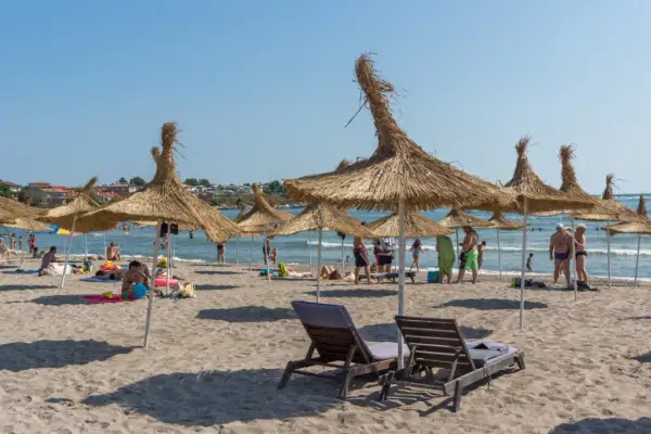 Słoneczna plaża z parasolami z trawy, leżakami i ludźmi cieszącymi się wakacjami. To idealne miejsce na **carewo atrakcje**.