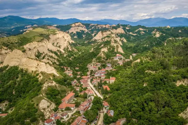 Malowniczy widok na Melnik w Bułgarii, z domami z czerwonymi dachami wciśniętymi między zielone wzgórza i skalne formacje.
