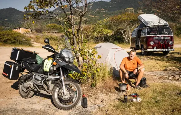 Motocykl, namiot i kamper to idealny zestaw, by wiedzieć, co zabrać na camping. Mężczyzna gotuje na kuchence turystycznej.